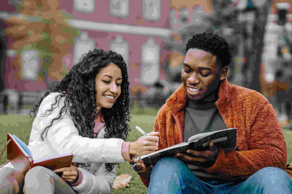 Two students sit next to one another outside.